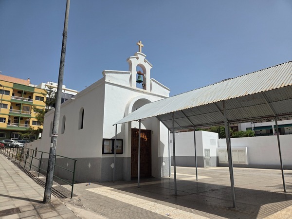 Pequeña iglesia blanca con campana y cruz en la entrada del pueblo.