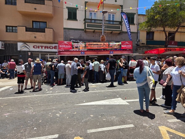 Fila de gente en un ventorrillo con carpas rojas en plena romería.