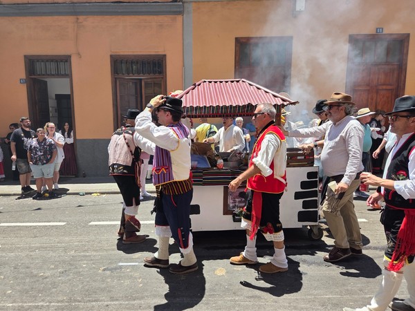 Romeros empujan un pequeño carro con tejadillo mientras preparan asados.