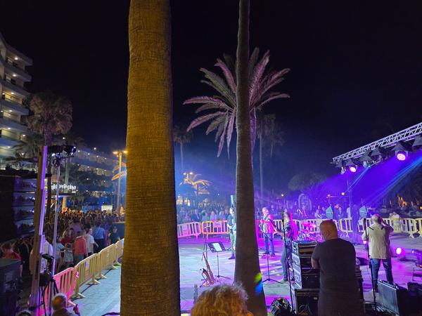 Concierto en directo con luces violetas y palmeras de fondo que ameniza la fiesta de San Juan.