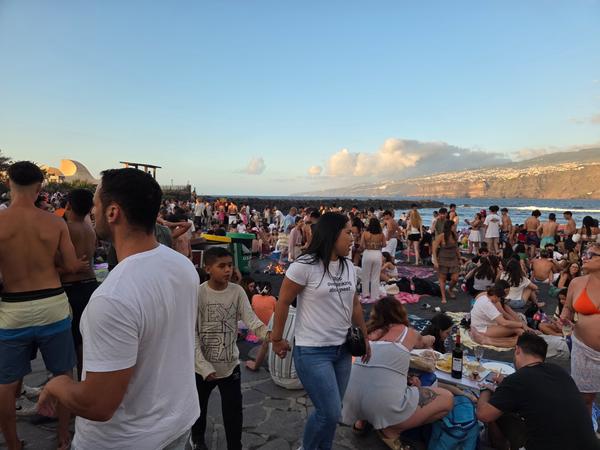Ambiente animado en la arena con grupos de amigos y familias esperando la caída del sol en la Noche de San Juan.