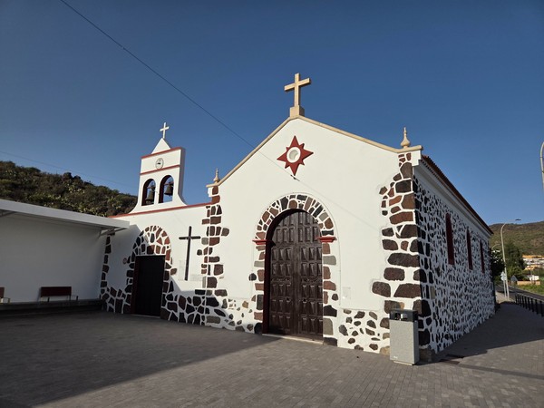 Fachada blanca de la iglesia de Santiago Apóstol con campanario y plaza engalanada.