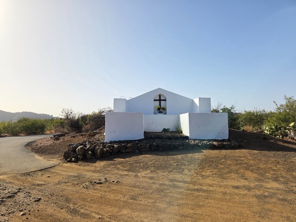 Pequeña capilla blanca con cruz en la ventana, rodeada de matorral canario.