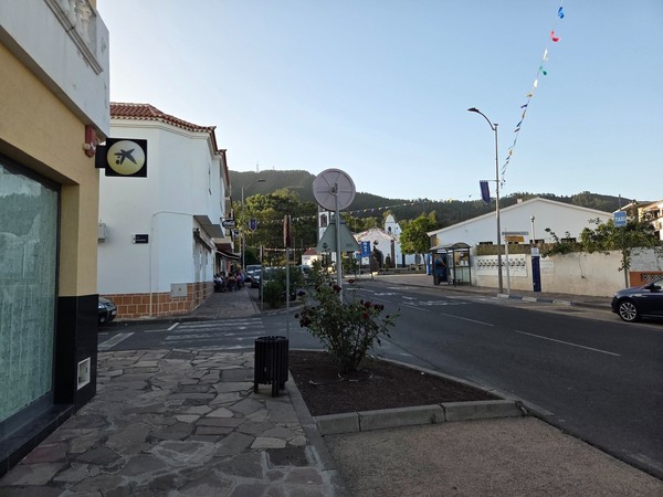 Calle principal de Santiago del Teide con parada de guagua, bancos y la iglesia al fondo decorada con banderines.