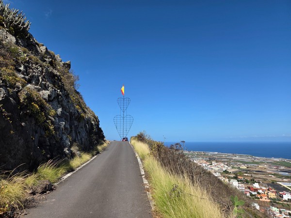 Estructura metálica en forma de corazones con bandera de España en un estrecho camino de la ladera sobre Tejina.