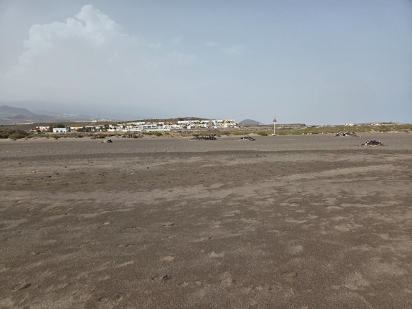 Superficie de arena volcánica y formaciones naturales en La Tejita con el complejo de Sotavento al fondo